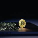 Bitcoin coin near laptop on black background. Finance and crypto money concept.