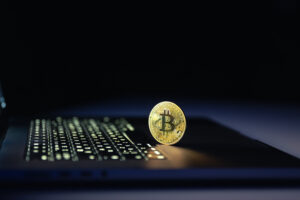 Bitcoin coin near laptop on black background. Finance and crypto money concept.